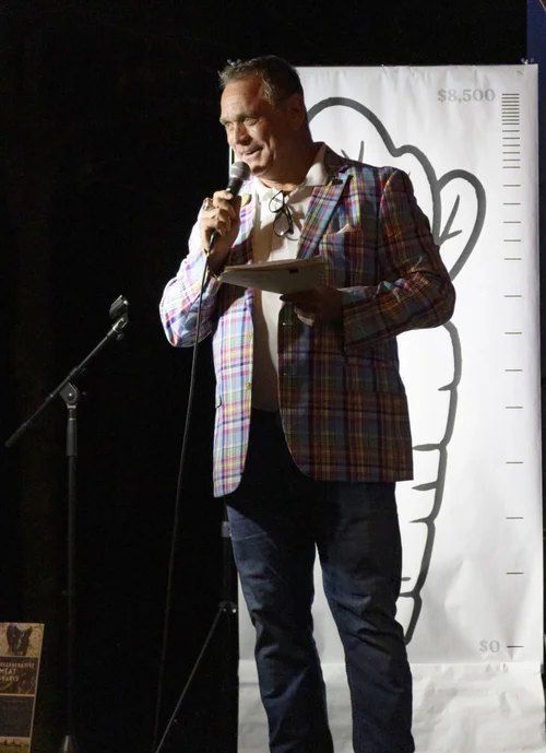 Todd Nichols at the microphone with his notes, in front of a fund-a-need goal thermometer